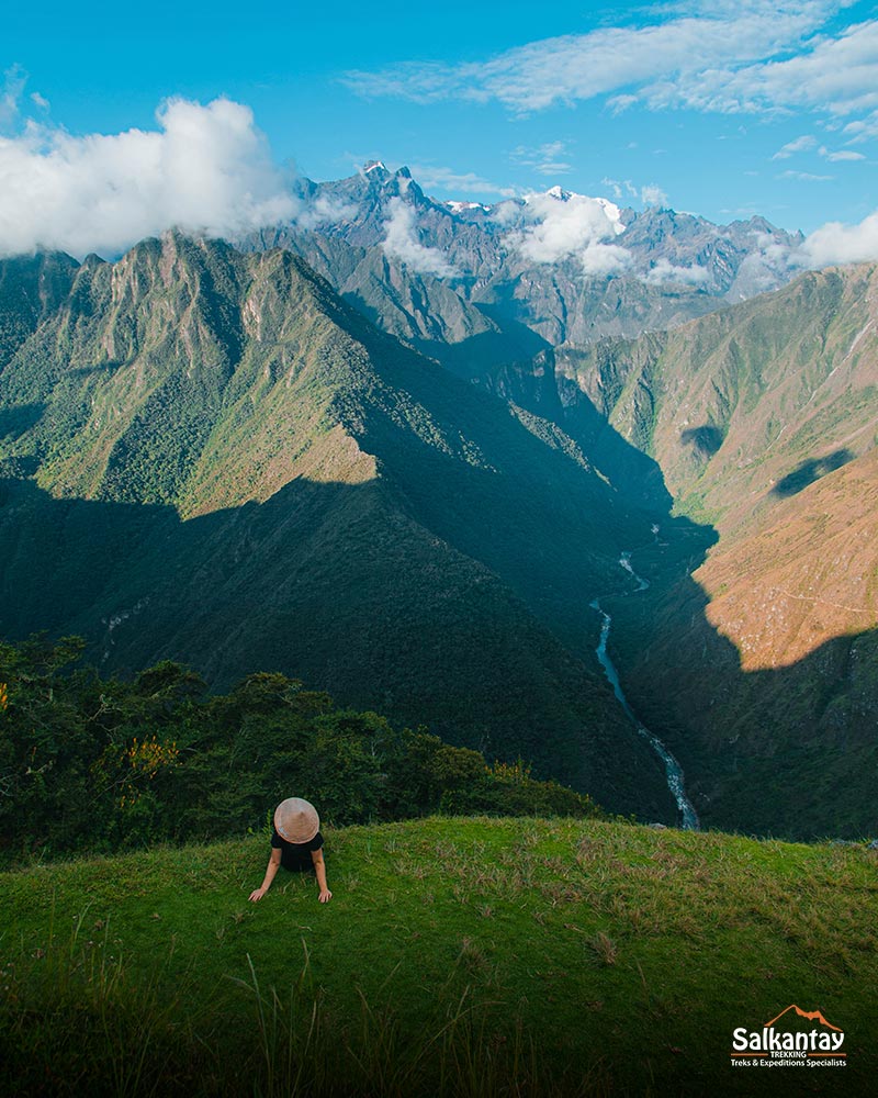 Female tourist sitting on the grass admiring the great and impressive Andean mountains on the Inca trail route.