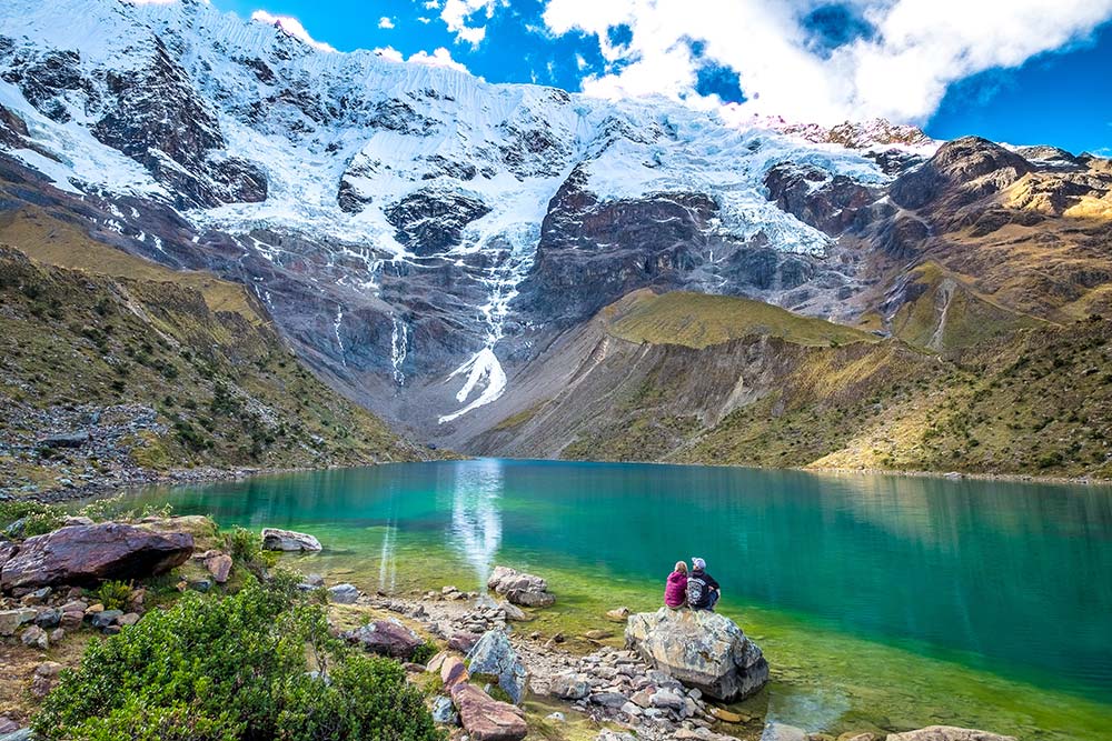 A tourist couple sitting on the shores of the Humantay Lagoon and the Turquoise Jewel.