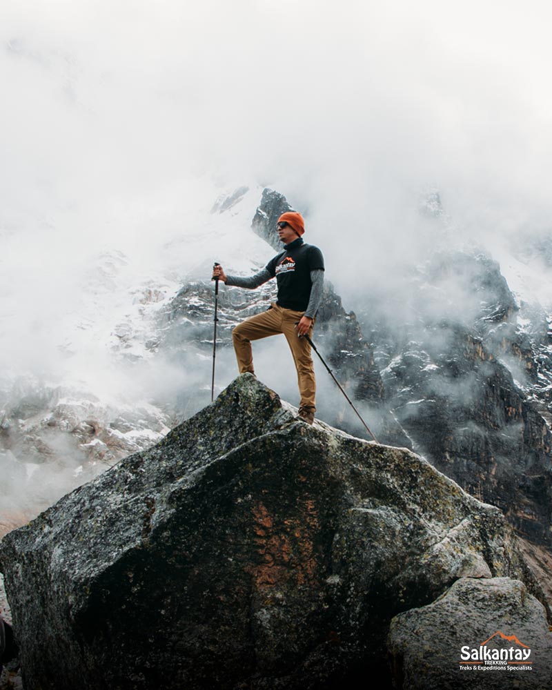 Tourist on top of a giant boulder with hiking poles on the Salkantay Pass