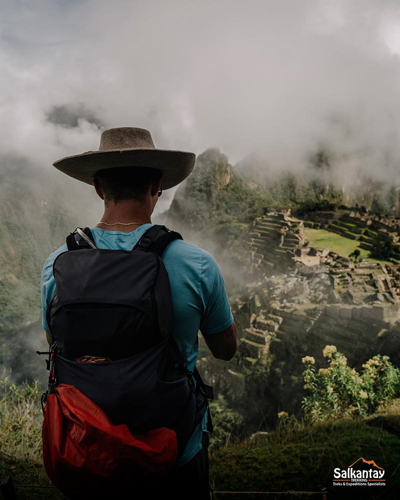 Male tourist with Andean hat admiring the Inca city of Machu Picchu full of clouds.