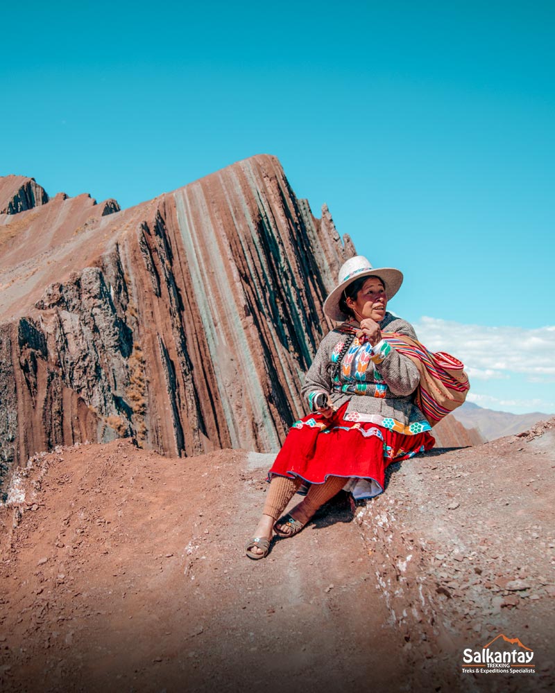 A person sitting in front of the mountain of colors of Pallay Punchu.