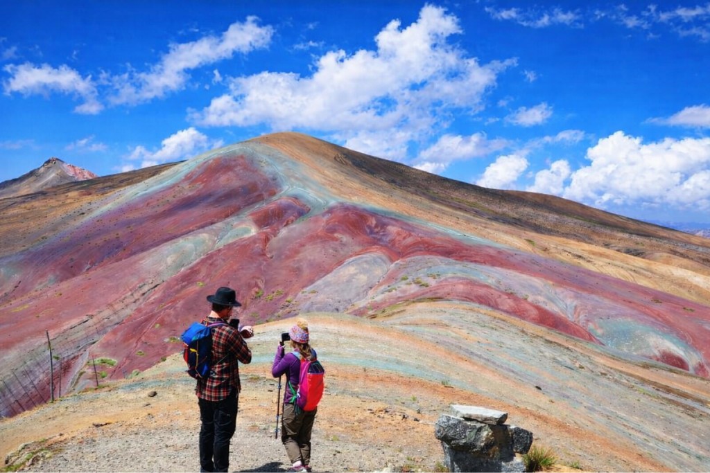 Two tourists taking photos of Wilcacuna Mountain, a colorful mountain in Peru - Colorful Mountains Peru