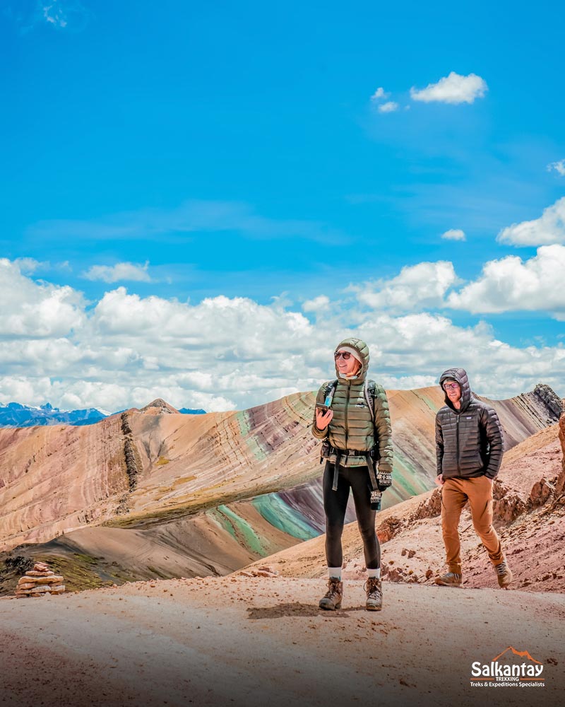 Two tourists walking in Palccoyo with a colorful mountain backdrop