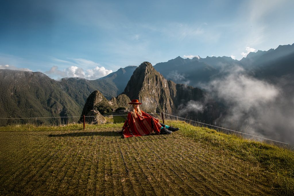 Tourist wearing a red Andean poncho with the Inca citadel of Machu Picchu in the background.