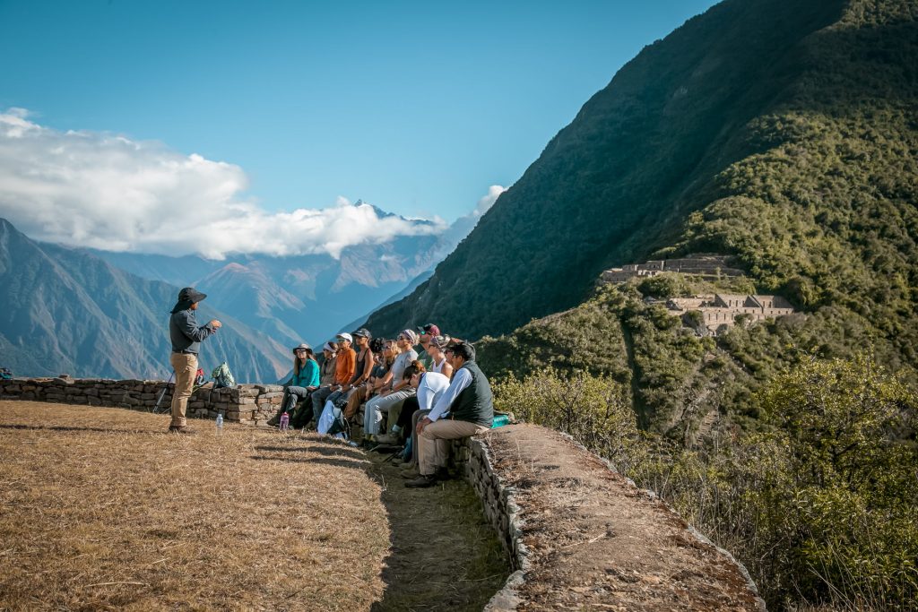 Panoramic photo of the archaeological site of Choquequirao with a group of tourists and their guide explaining the site.