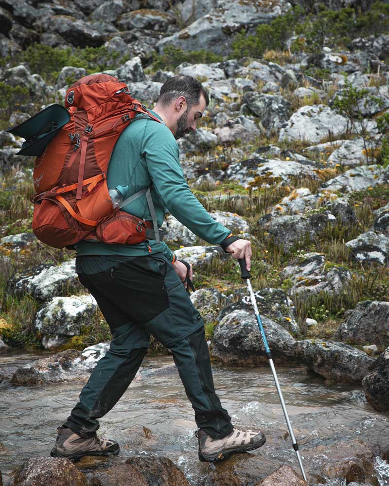 A hiker crossing a stream on the Salkantay Trek, equipped with trekking poles and a backpack that fits his build well