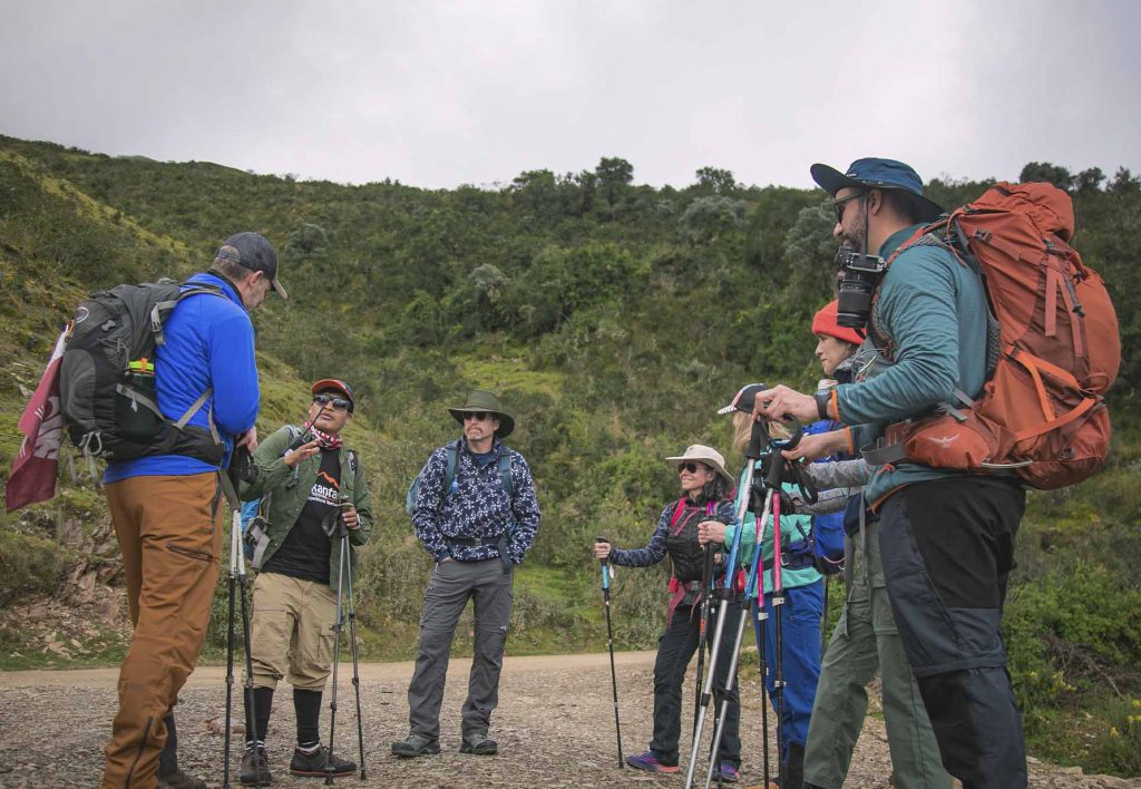 A group of tourists on the Salkantay Trail, carrying backpacks, wearing hats, and using trekking poles