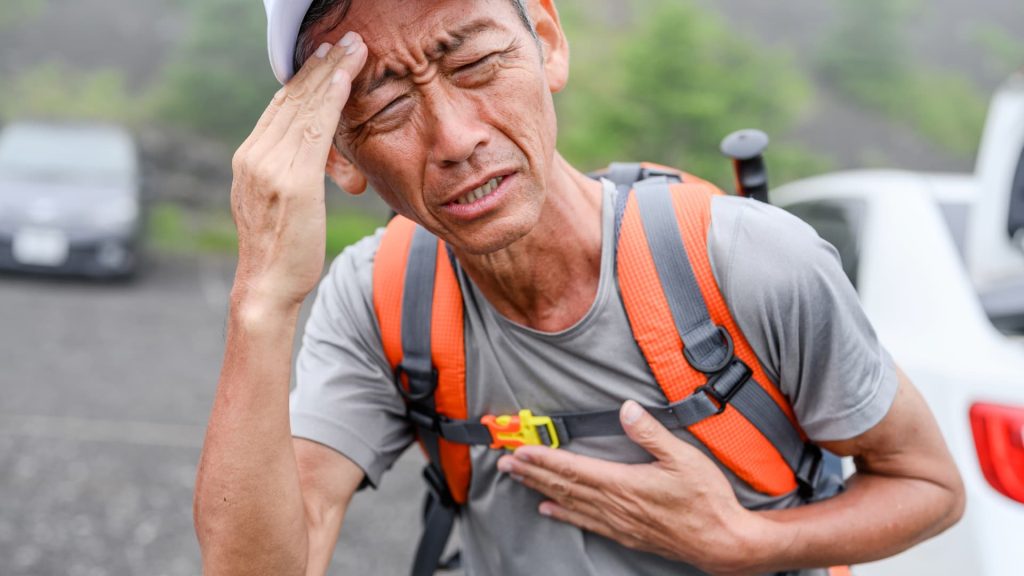 An exhausted hiker touching their forehead while resting on a high-altitude mountain peak.