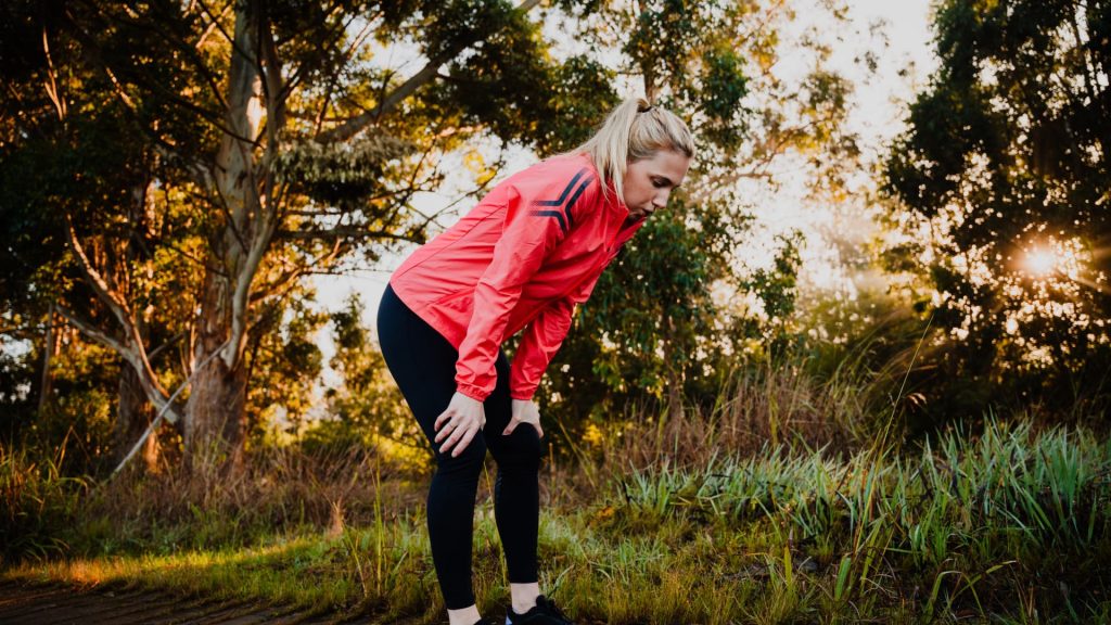 Person bent over with hands on knees catching their breath during an intense workout session.