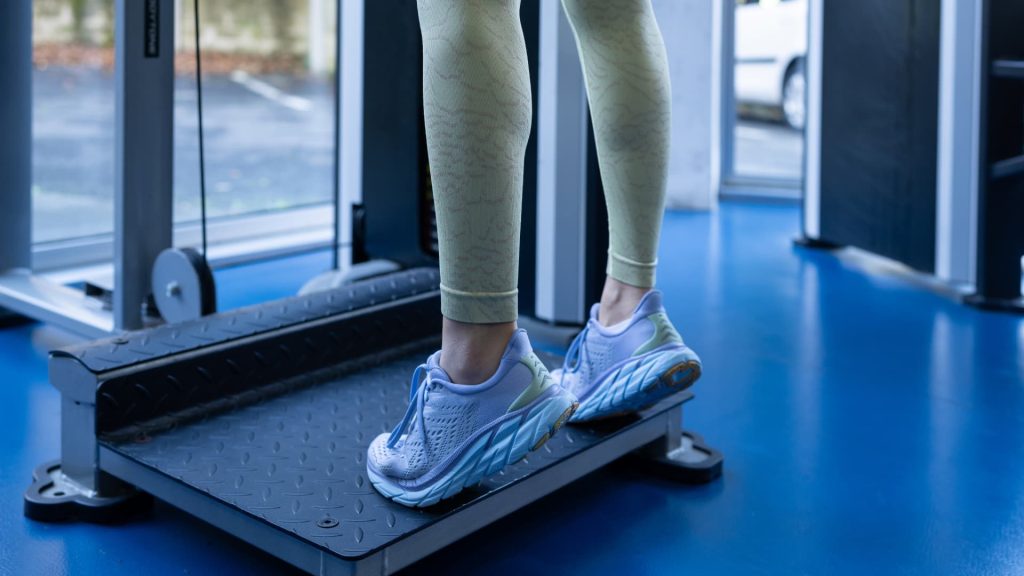 Close-up of a person performing standing calf raises on an elevated platform in a gym.