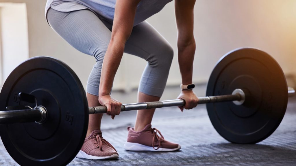 Close-up of a person gripping a loaded barbell, preparing to perform a deadlift exercise in a gym.