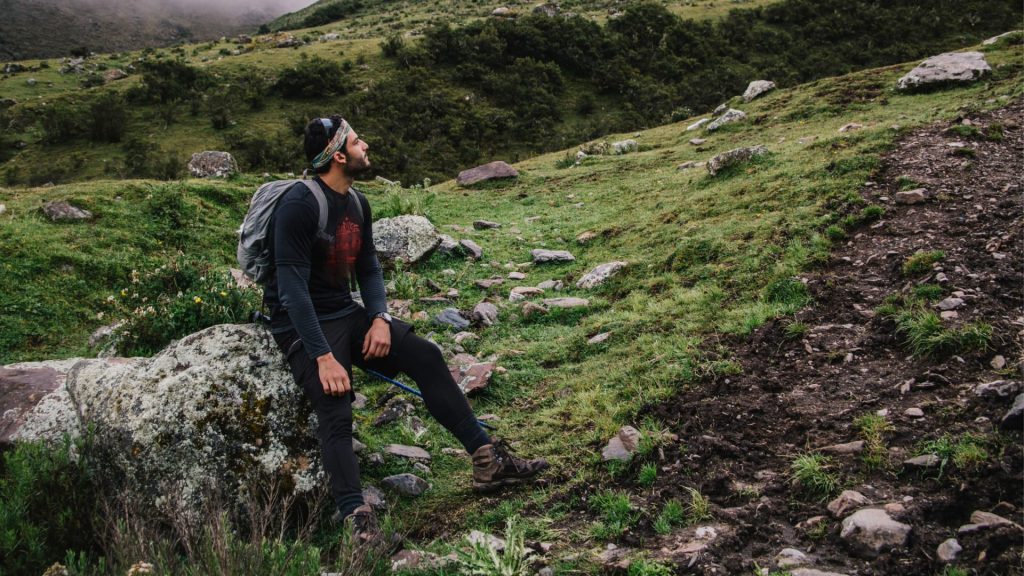 A tired person wearing a backpack resting on a rock during a demanding high-altitude mountain hike.