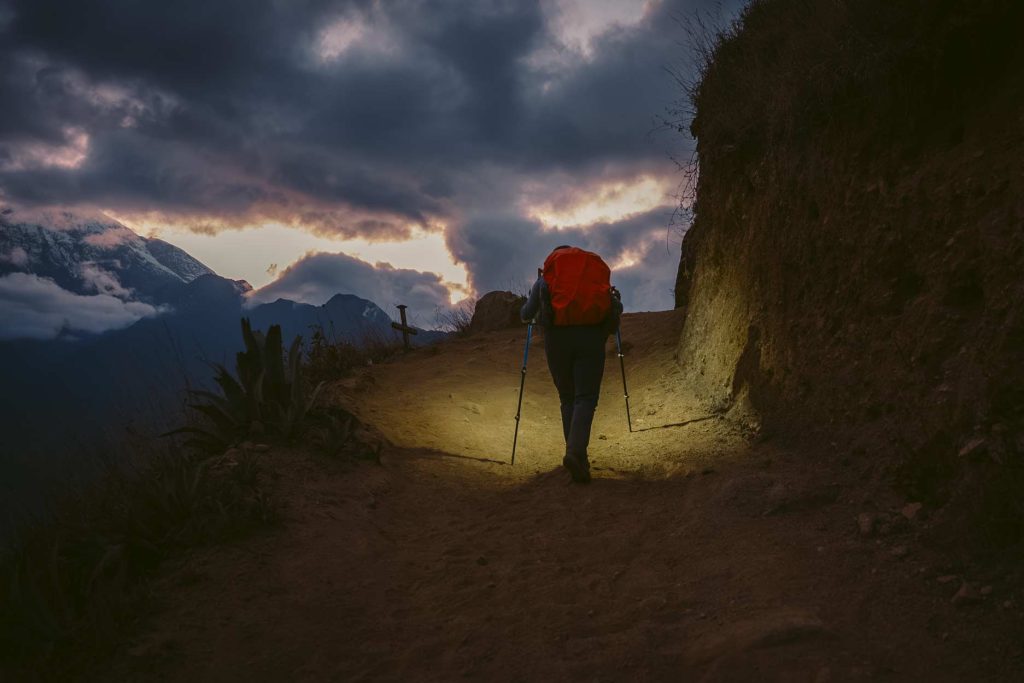 A tourist walking with a flashlight at sunset on the hike to Choquequirao