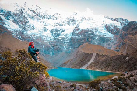 Impressive view of the mountain and Humantay lagoon and a tourist sitting enjoying the landscape