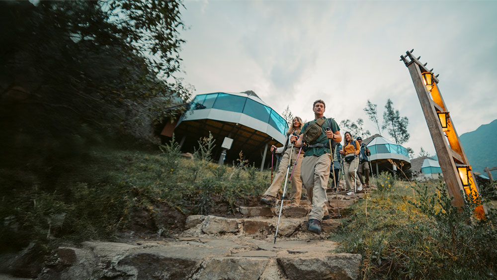 A group of hikers with backpacks arriving at the luxury Mountain Sky View camp, featuring modern glass domes and a stunning view of the Andean mountains in the background.