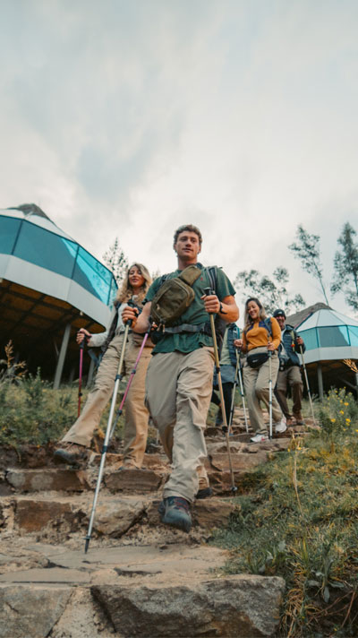 A group of hikers with backpacks arriving at the luxury Mountain Sky View camp, featuring modern glass domes and a stunning view of the Andean mountains in the background.