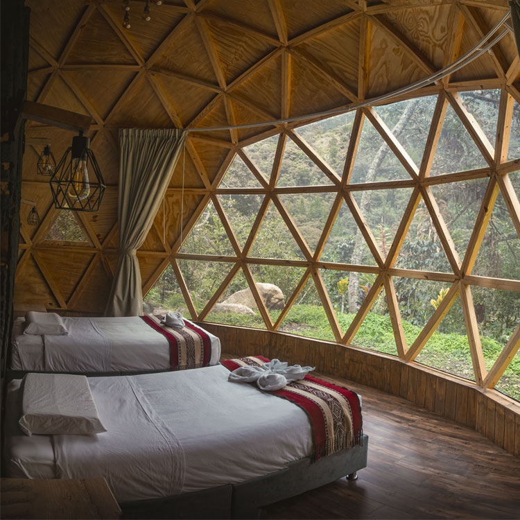 The elegant interior of a suite at Sacred Jungle Lodge, featuring warm wooden walls, a cozy bed with Andean textiles, and large floor-to-ceiling windows overlooking the tropical forest.