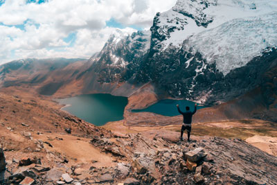 Impressive panoramic view of a tourist raising his hands looking at the Ausangate mountain and its turquoise lakes.