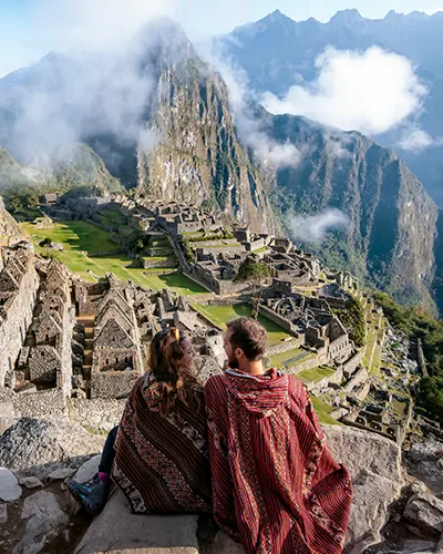 Tourist couple dressed in Andean ponchos in front of Machu Picchu