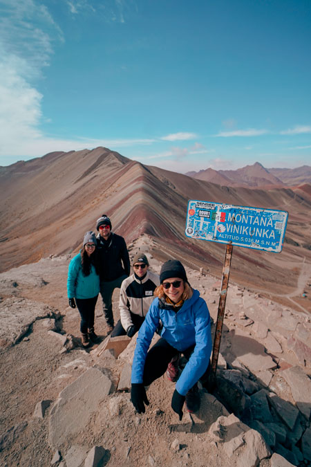 Four tourists passing by for the photo with the background of the Vinicunca rainbow mountain.