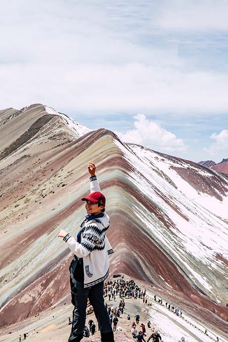 Tourist raising his hand in front of the rainbow mountain of Vinicunca