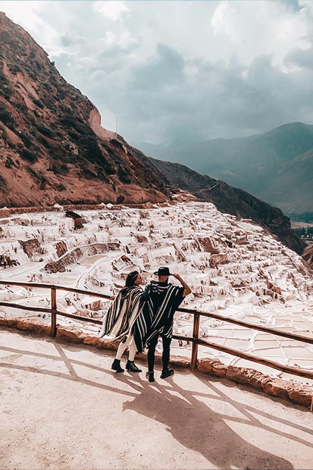 A tourist couple with Andean ponchos watching the salt mines of Maras.
