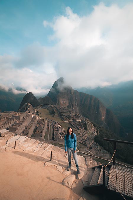 Tourist posing for the photo with the background of Machu Picchu with some clouds.