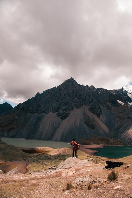 Tourist in red Andean poncho looking at turquoise lakes in the background