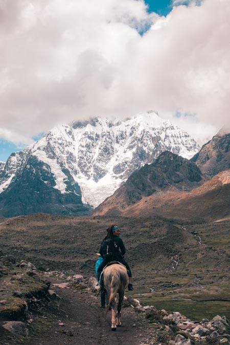 Tourist riding a horse in the direction of the great Ausangate mountain.