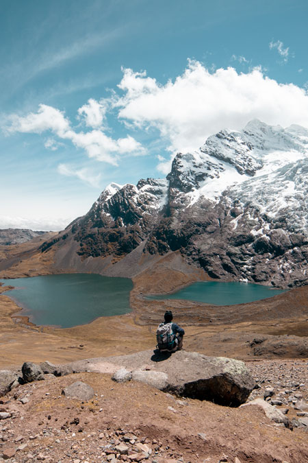 Tourist sitting on a rock looking at the lagoons found in the Ausangate mountain.