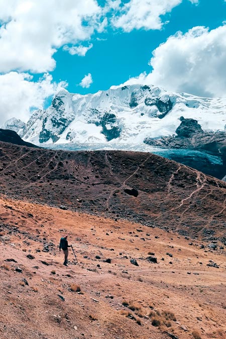 A tourist walking downhill against the white backdrop of Ausangate mountain.