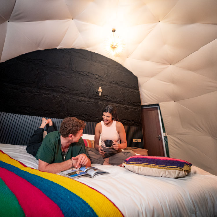 A young couple enjoying the comfort of their exclusive suite at the Super Jungle Domes, surrounded by the lush green foliage of the Peruvian cloud forest in Lucmabamba.
